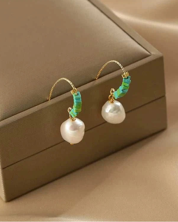Pearl earrings with green accents on a beige jewelry box