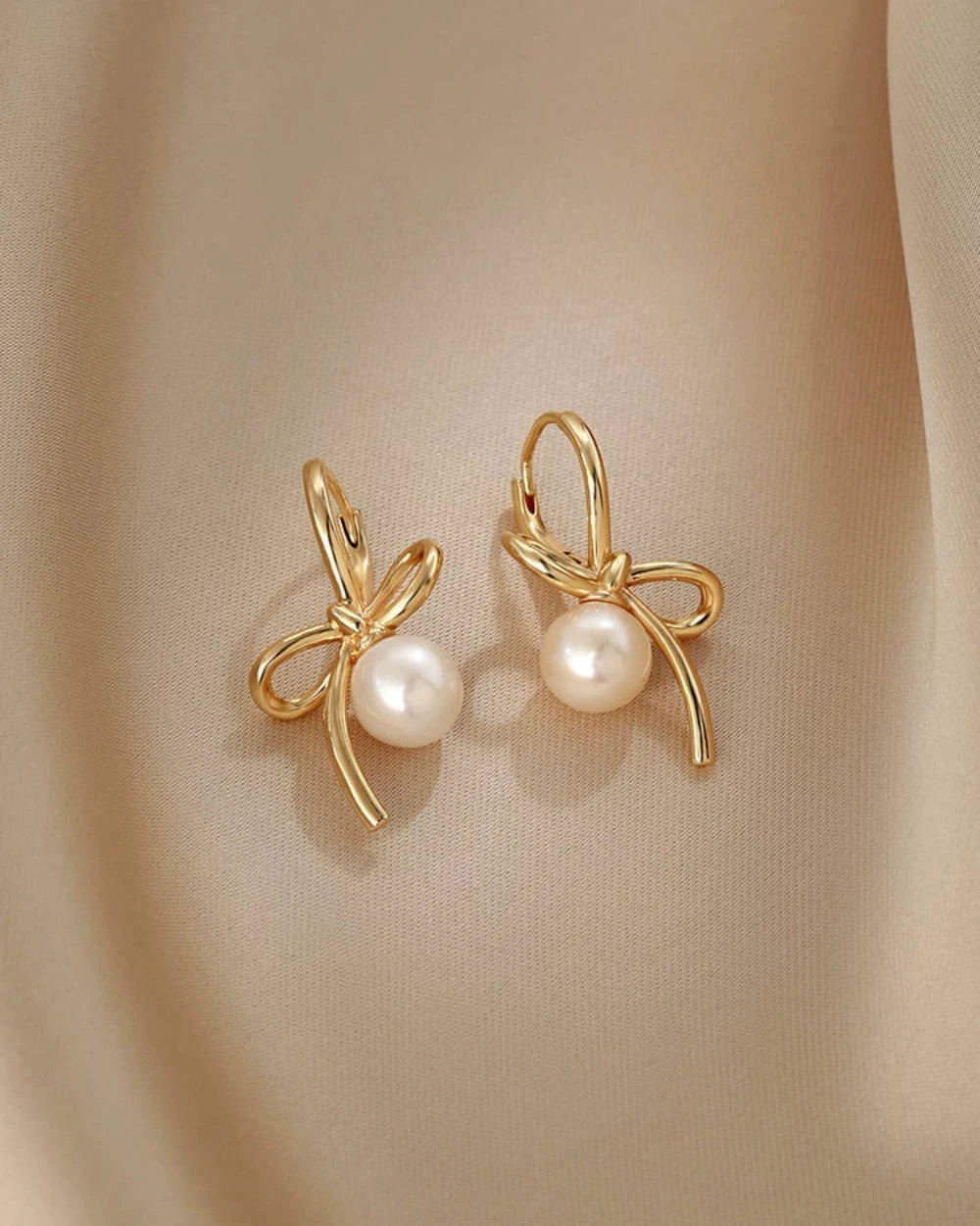 Gold bow-shaped earrings with pearls on a beige background
