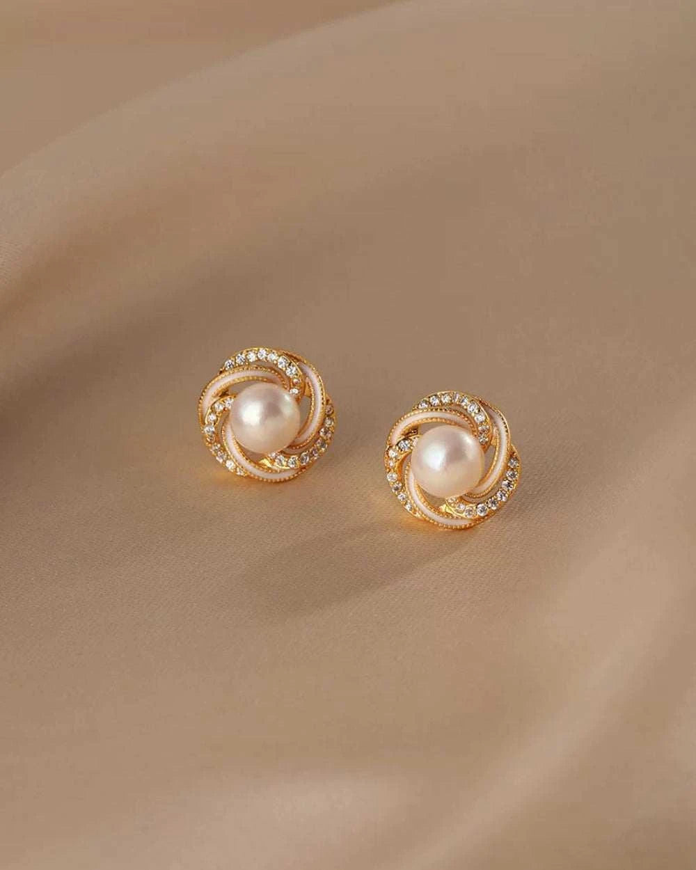 Pair of gold earrings with pearl center on a beige background