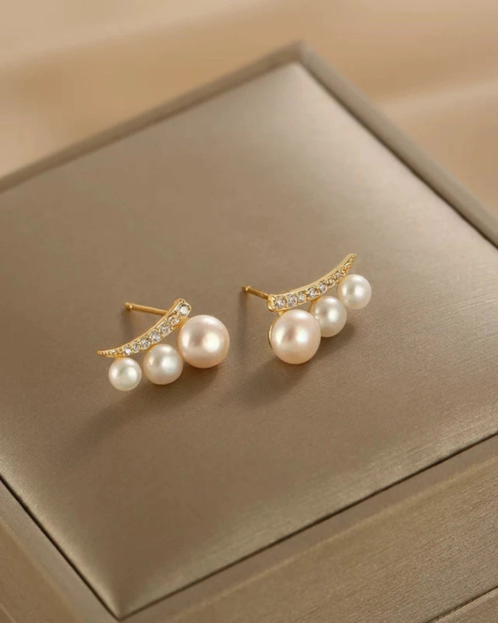 Pair of pearl earrings with gold accents on a beige jewelry box