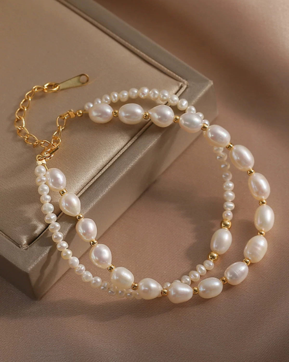 Pearl bracelet with gold chain on a beige surface