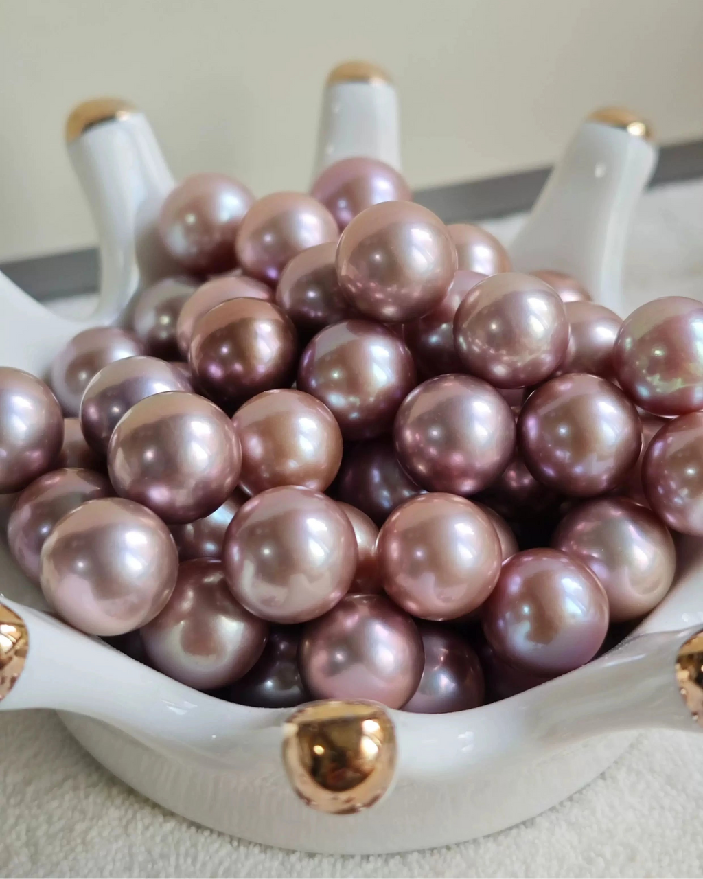 Pink pearls in a white dish with gold bases on a light background