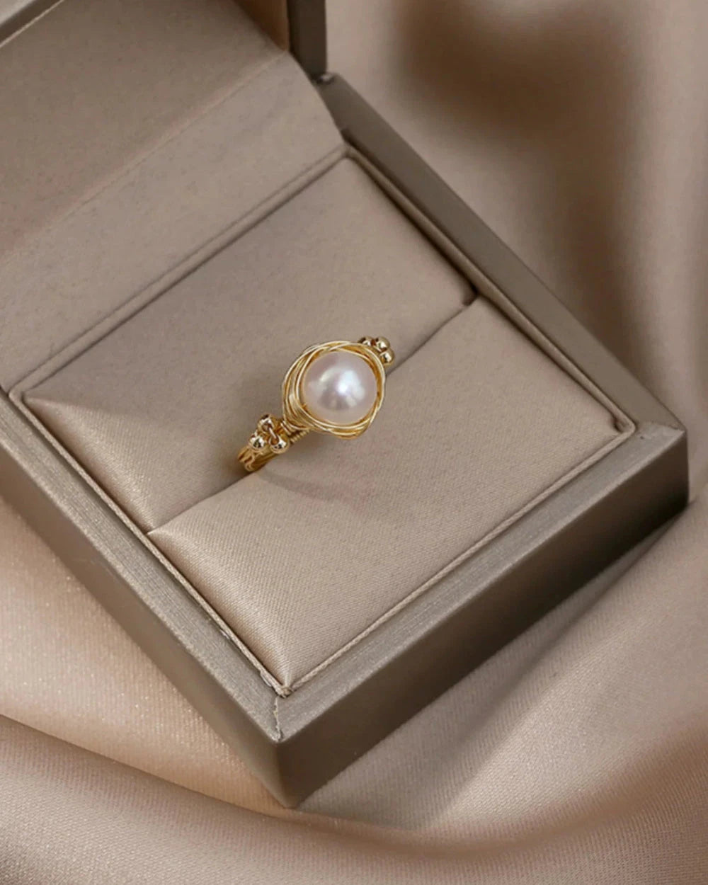 Gold ring with a pearl in a jewelry box on a beige fabric background