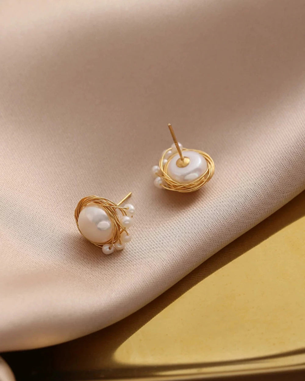 Pair of gold earrings with pearls on a beige fabric background