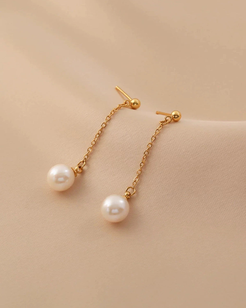 Pearl earrings with gold chains on a beige background