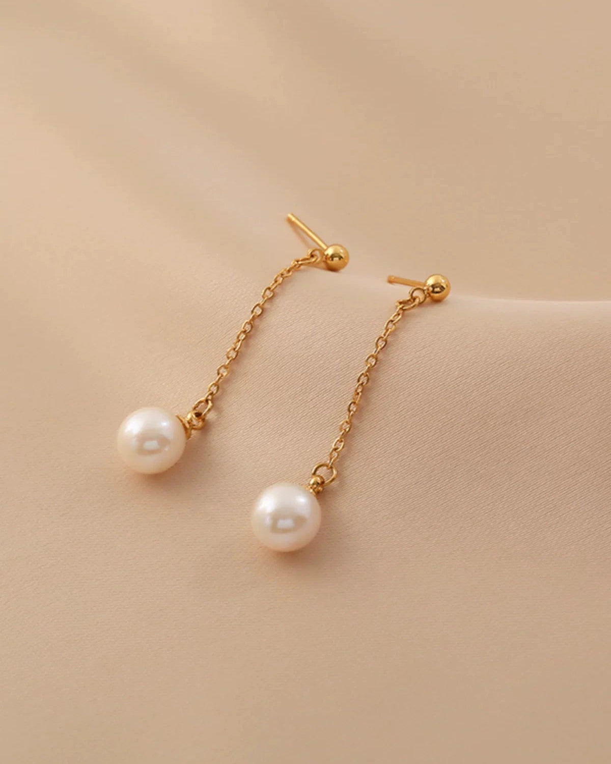 Pearl earrings with gold chains on a beige background