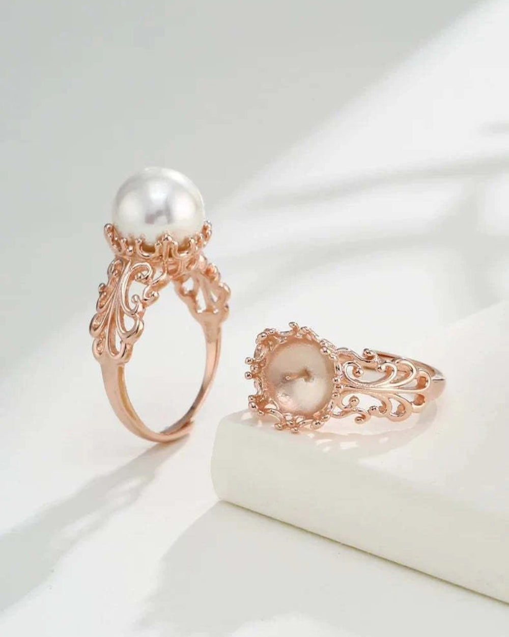 Two rose gold rings with pearls on a light background
