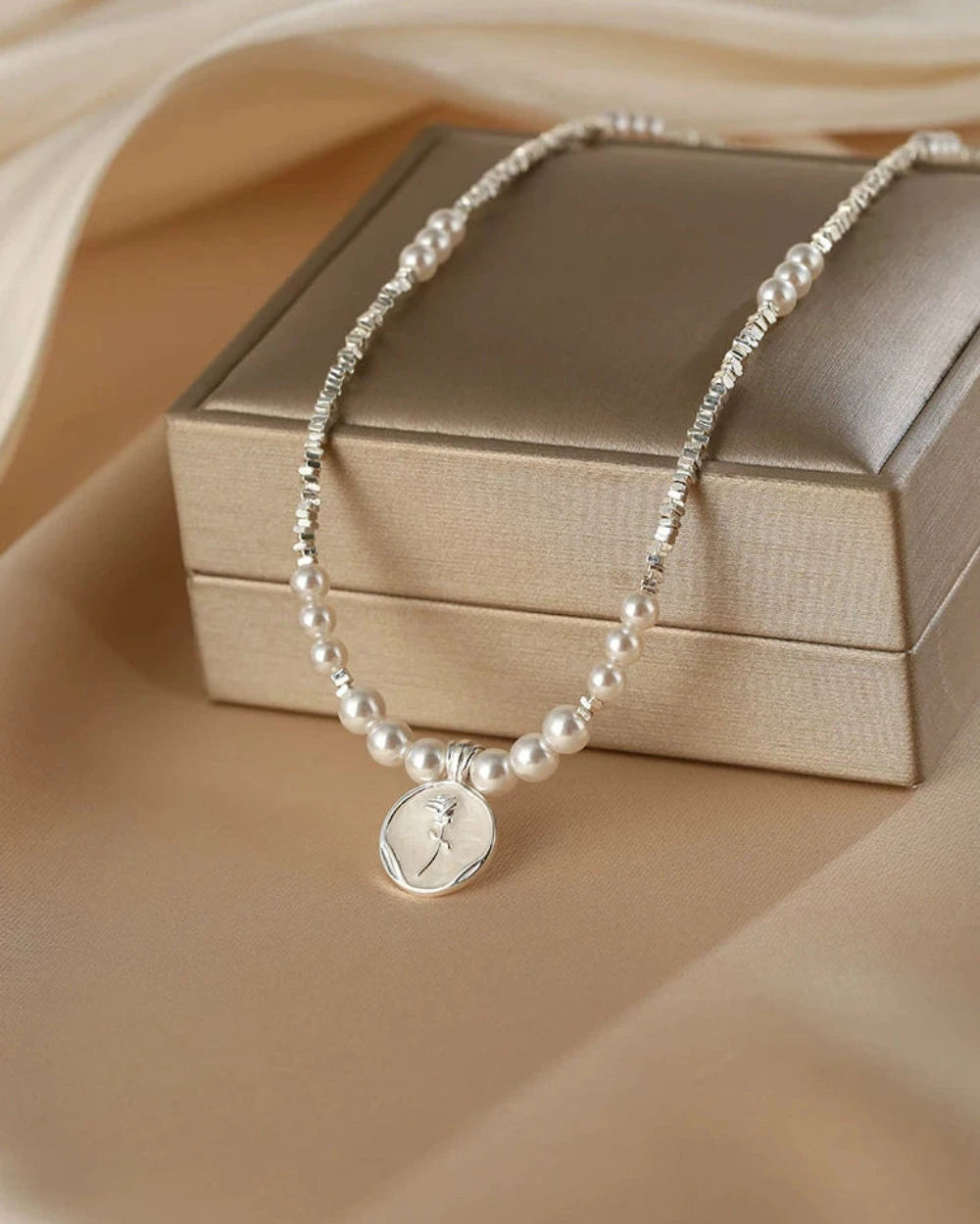 Pearl necklace with a silver pendant on a beige surface