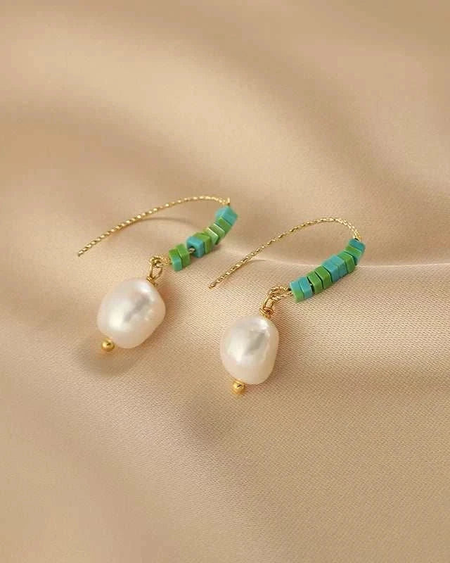 Pair of pearl earrings with green beads on a beige fabric background
