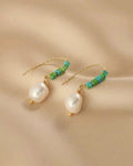 Pair of pearl earrings with green beads on a beige fabric background