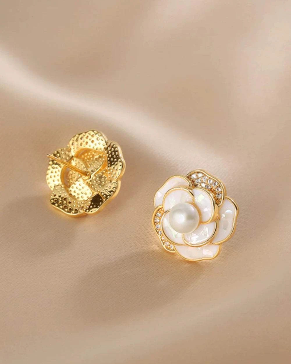 Gold and pearl flower-shaped earrings on a beige background