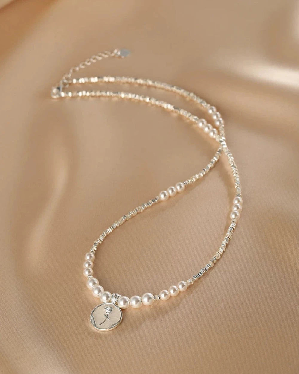 Pearl necklace with a silver pendant on a beige background