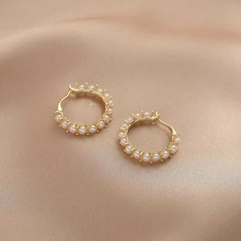 Gold hoop earrings with pearl accents on a beige fabric background