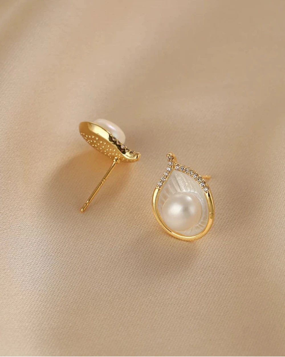 Gold earrings with pearl-like stones on a beige fabric background