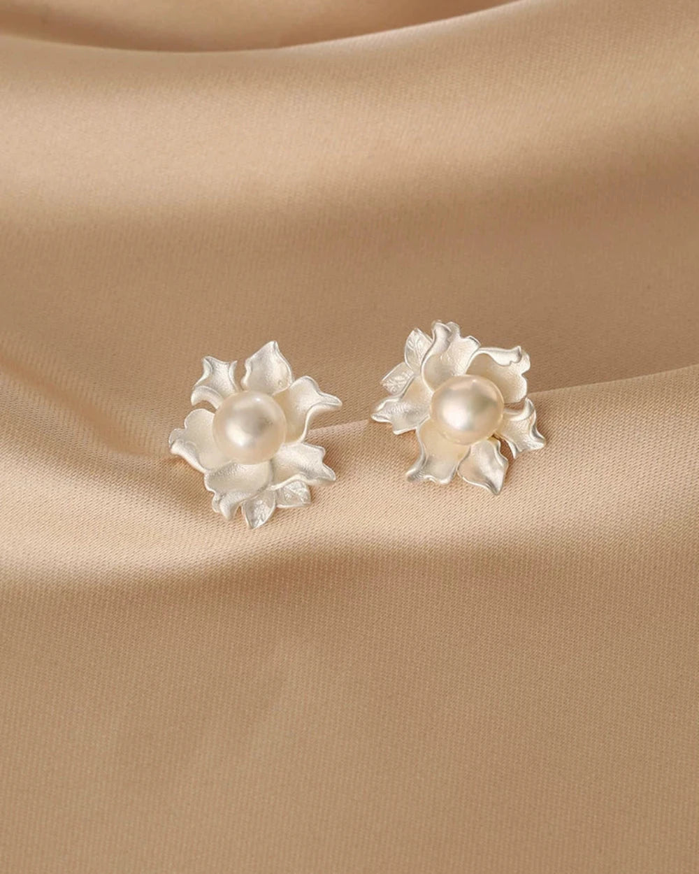 Pair of pearl earrings on a beige fabric background