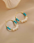 Gold hoop earrings with turquoise and pearl beads on a beige background