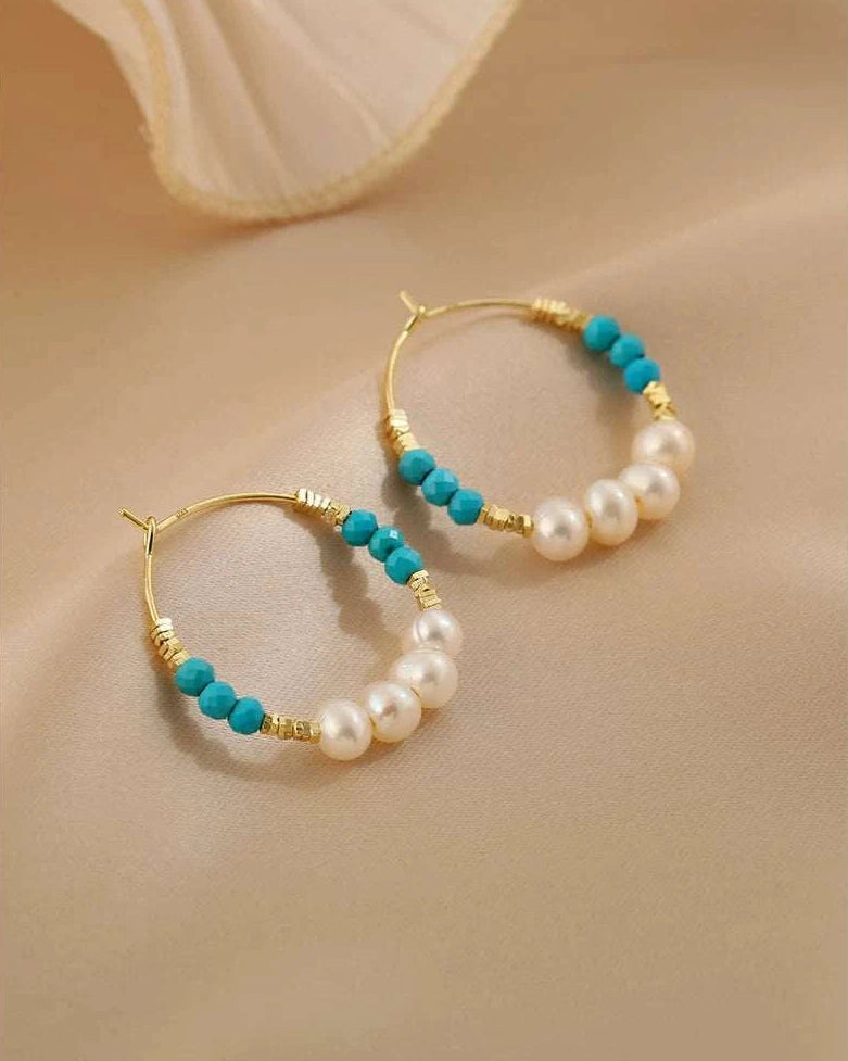 Gold hoop earrings with turquoise and pearl beads on a beige background