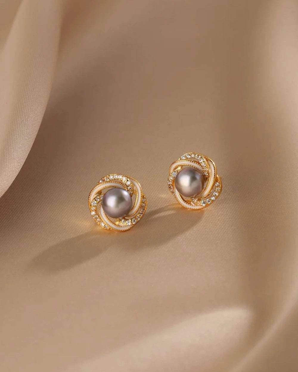 Pair of gold earrings with gray pearls on a beige fabric background