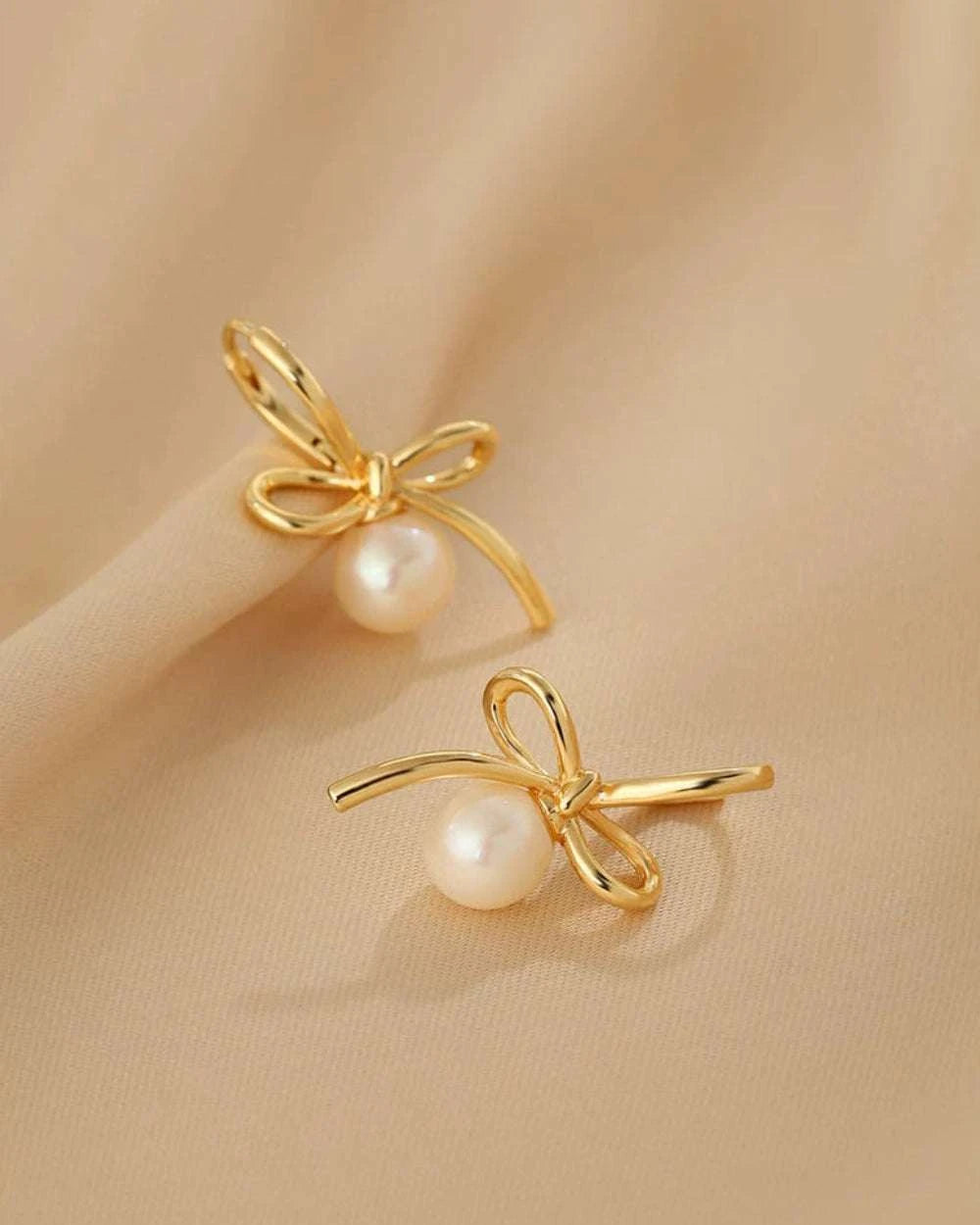 Gold bow-shaped earrings with pearls on a beige background
