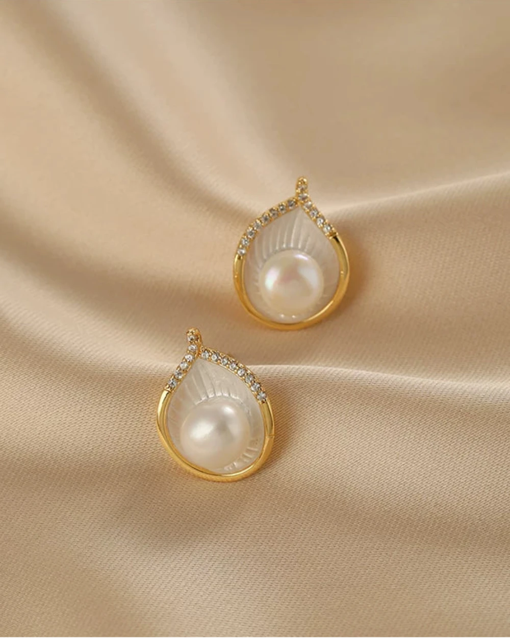 Pair of pearl earrings with gold accents on a beige fabric background