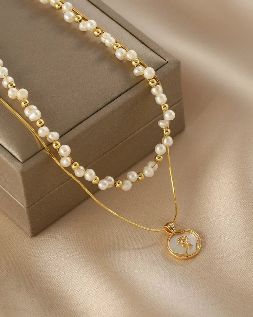 Pearl necklace with a gold chain and pendant on a beige surface