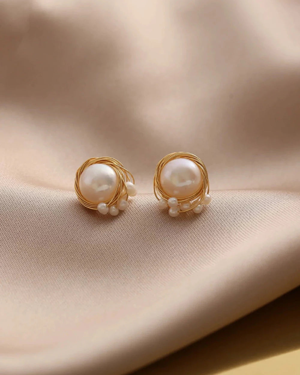 Pearl earrings with gold wire wrapping on a beige fabric background