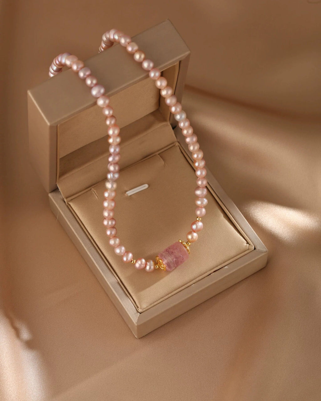 Pearl necklace with a pink pendant on a beige jewelry box