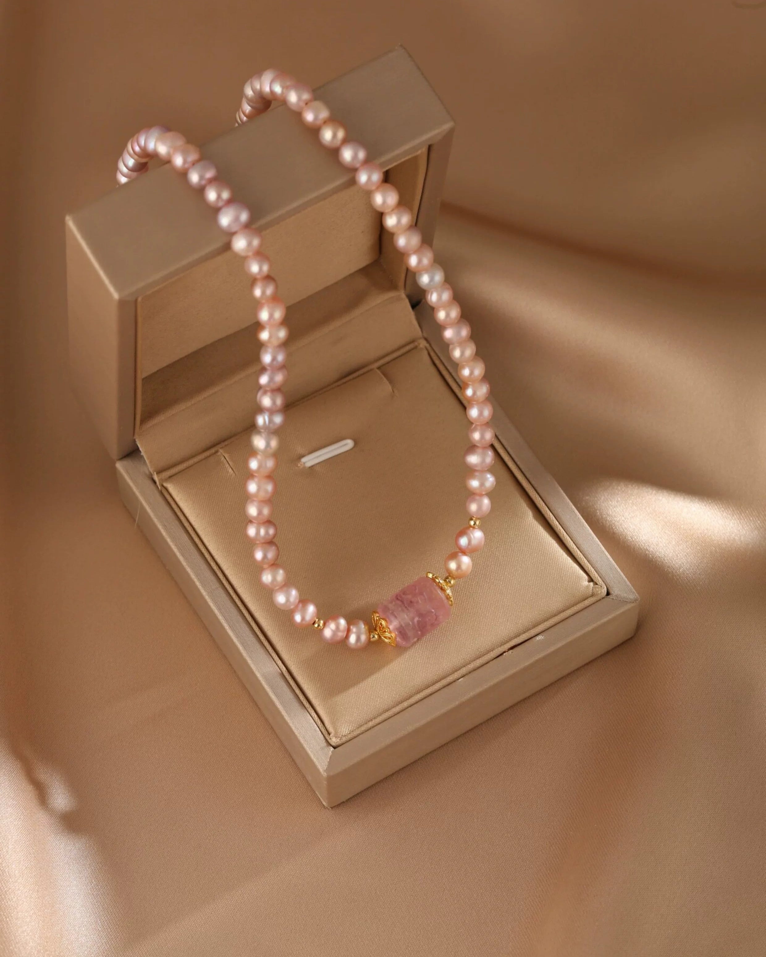 Pearl necklace with a pink pendant on a beige jewelry box