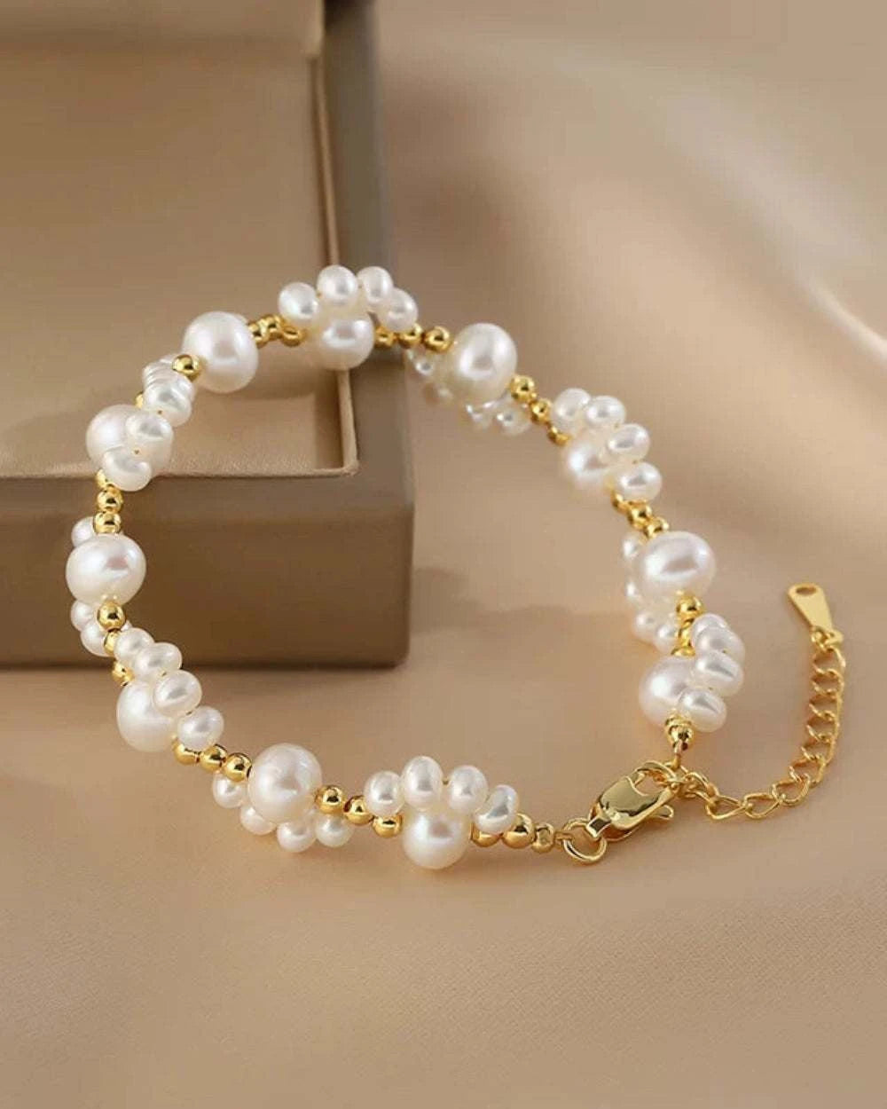 Pearl bracelet with gold chain on a beige background