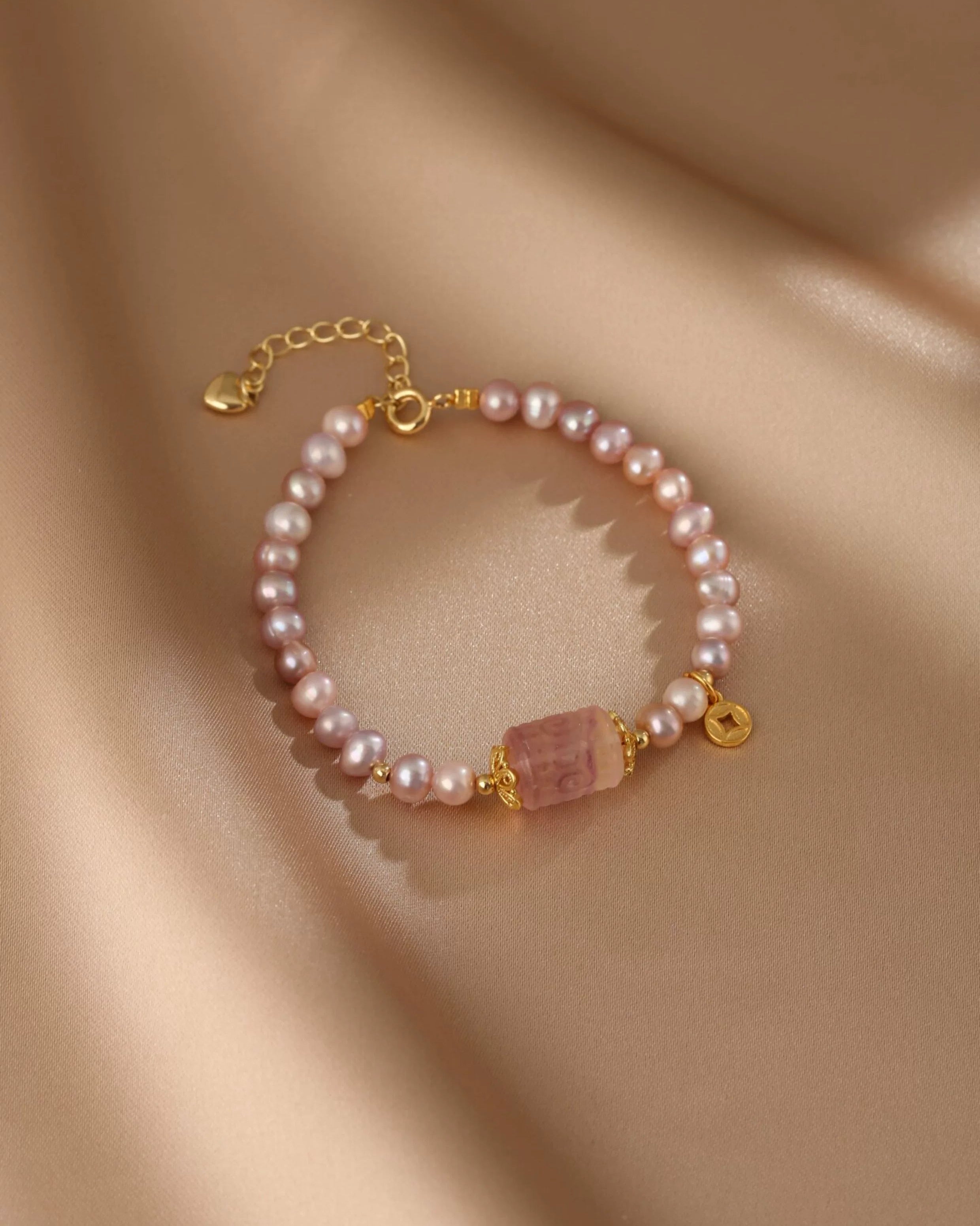 Pearl bracelet with a pink stone charm on a beige fabric background