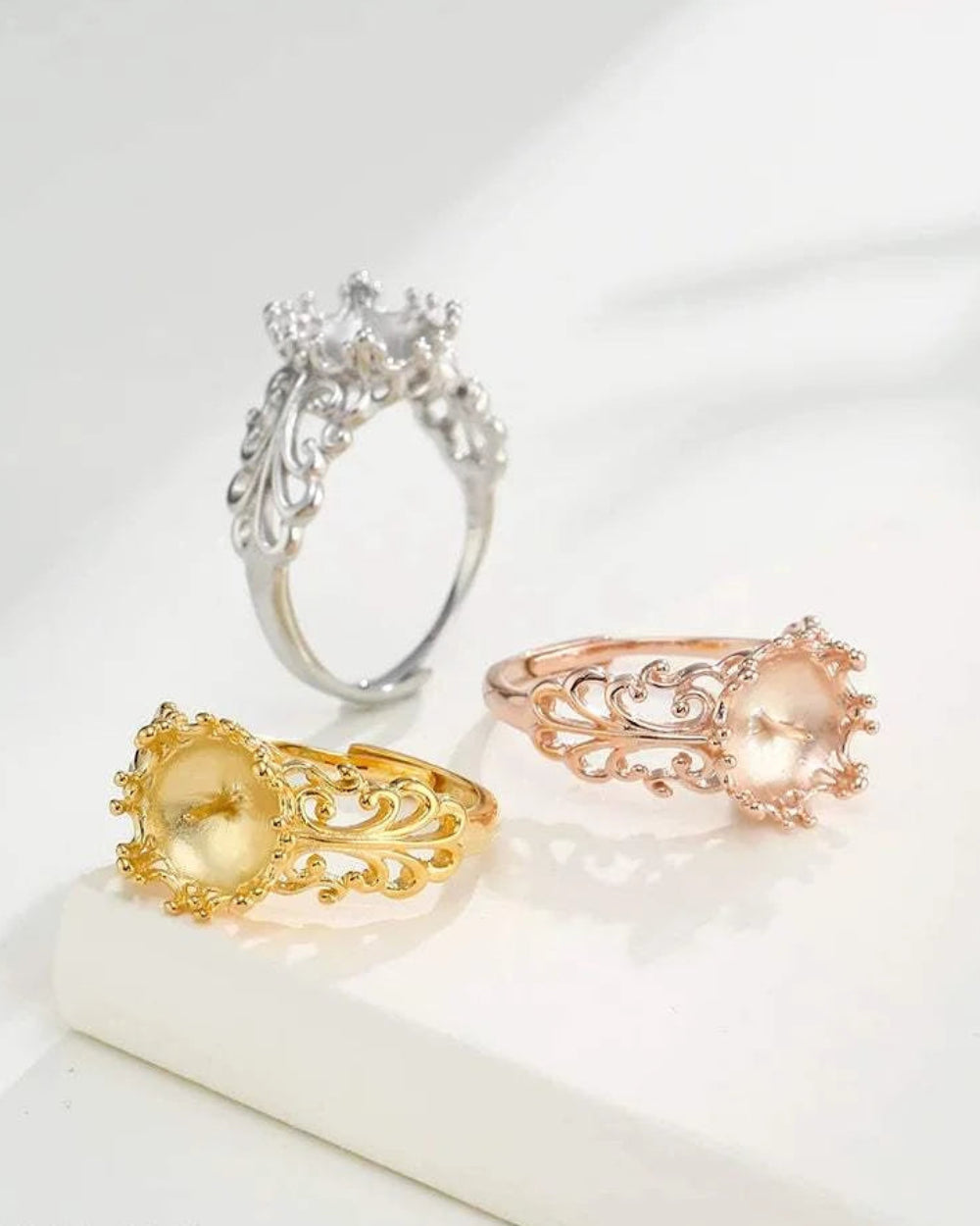 Three ornate rings in gold, silver, and rose gold on a light background