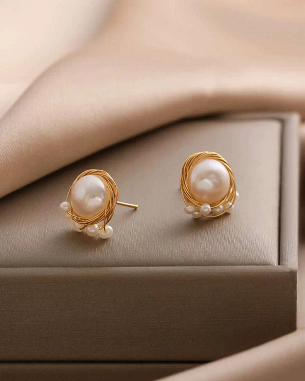 Pearl earrings with gold setting on a beige surface