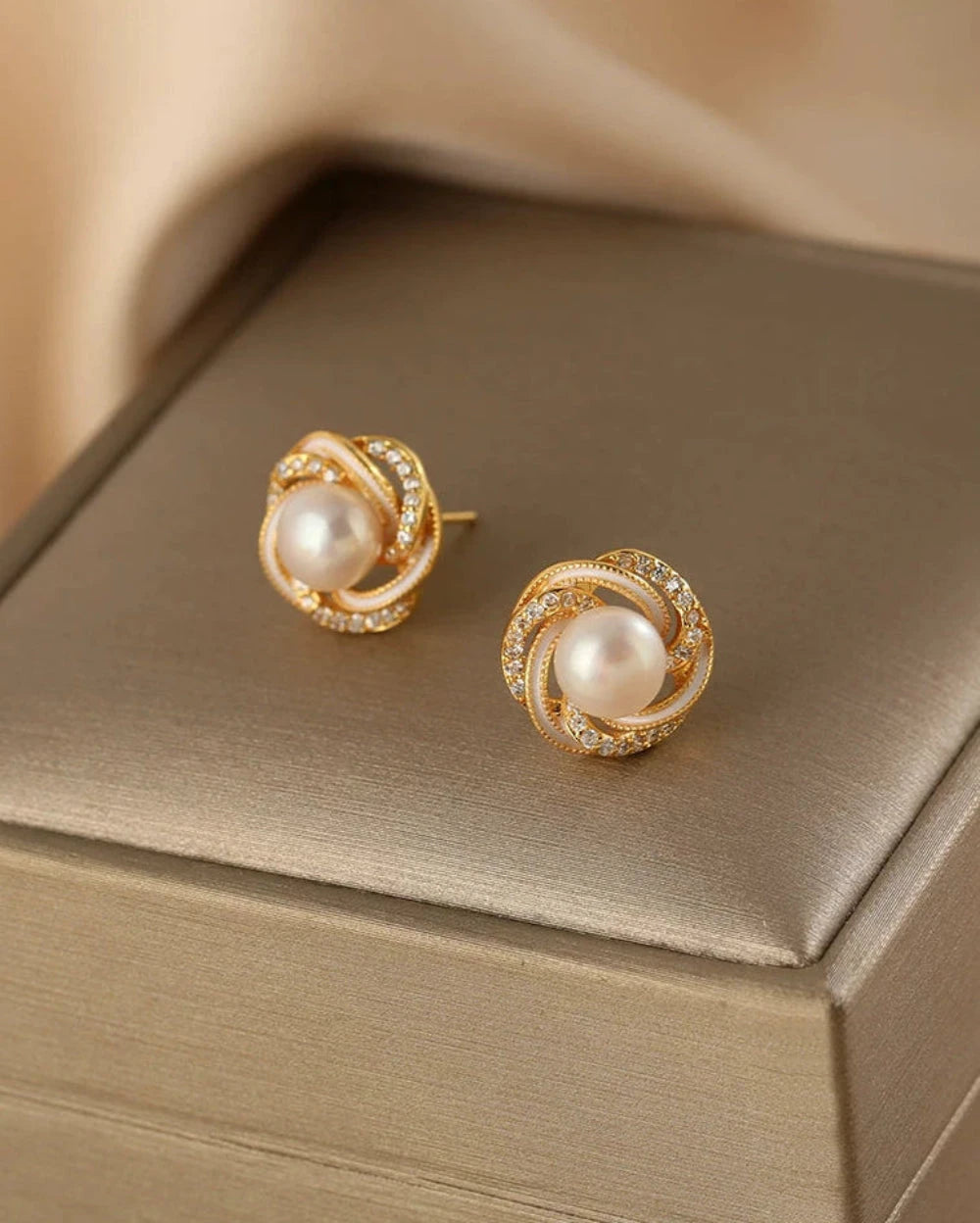 Gold earrings with pearls on a beige jewelry box