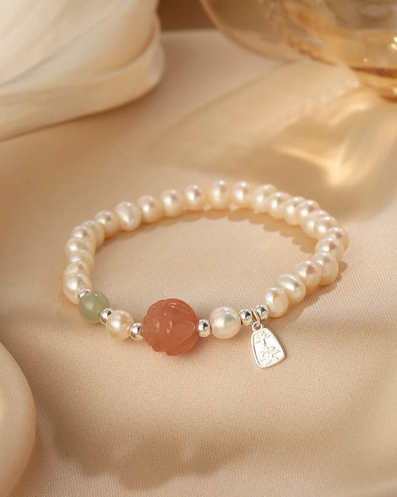 Pearl bracelet with a red stone and silver tag on a beige surface