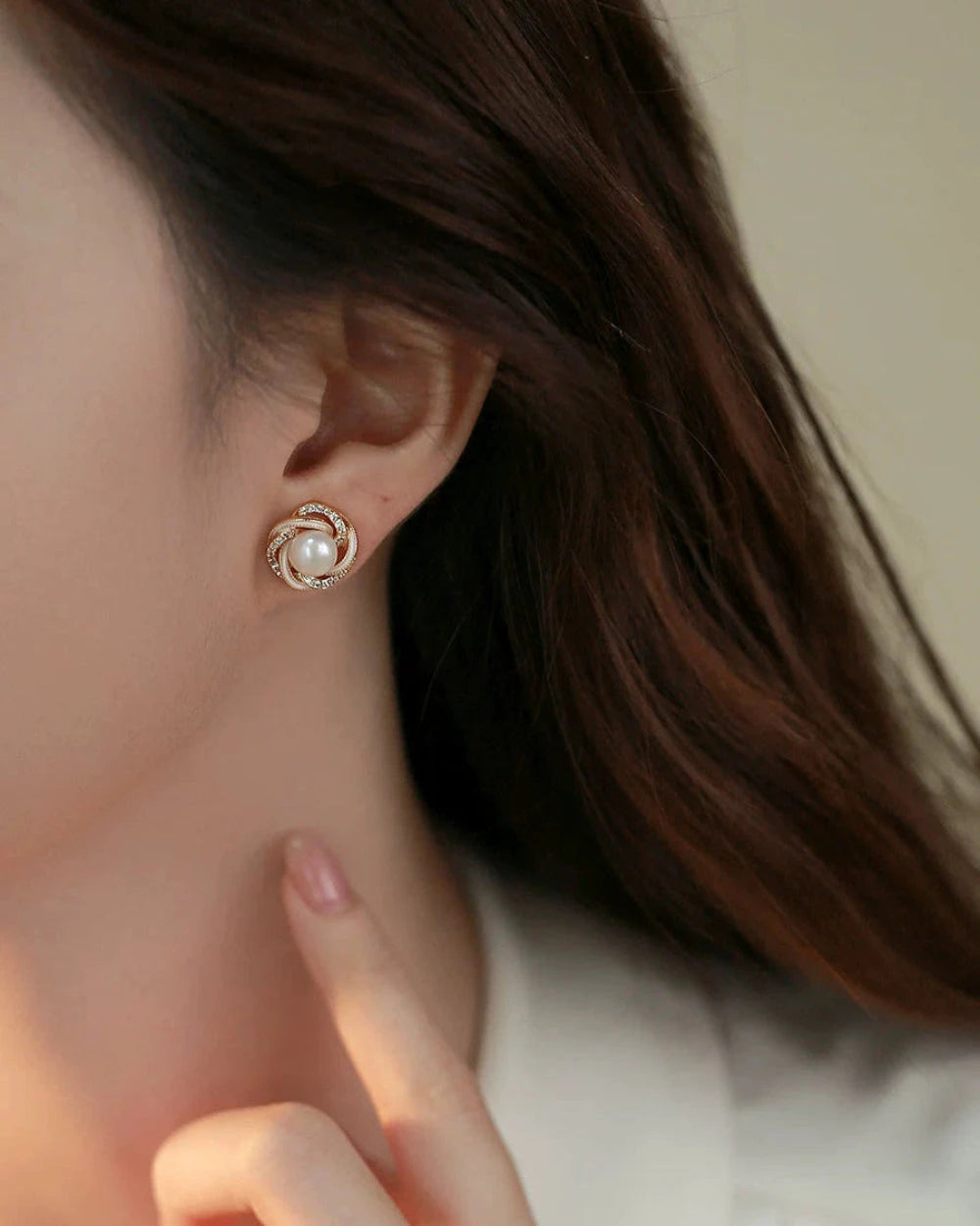 Close-up of a pearl earring worn by a person with brown hair.