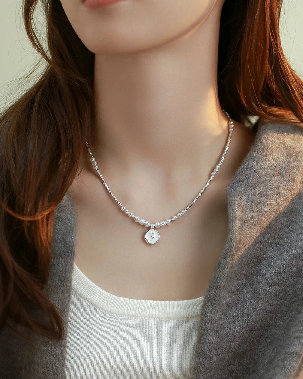 Necklace with a pendant on a mannequin wearing a gray cardigan and white top.