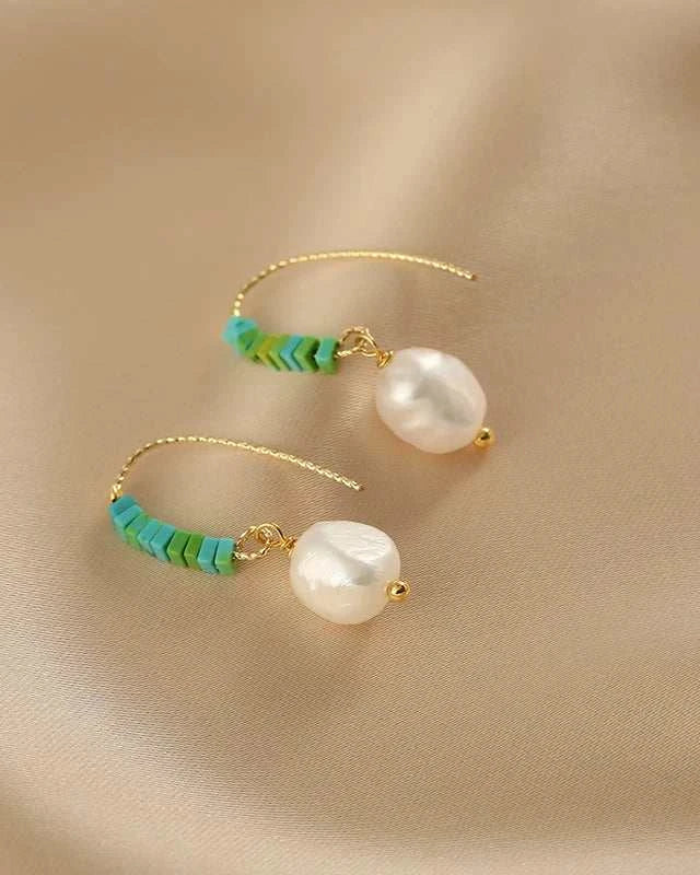 Pair of pearl earrings with turquoise beads on a beige fabric background