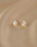 Pair of pearl earrings with gold accents on a beige fabric background