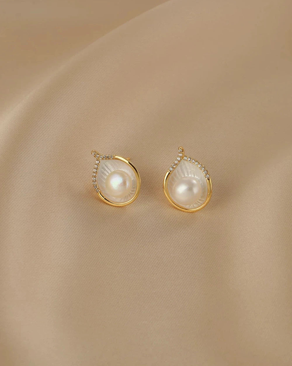 Pair of pearl earrings with gold accents on a beige fabric background