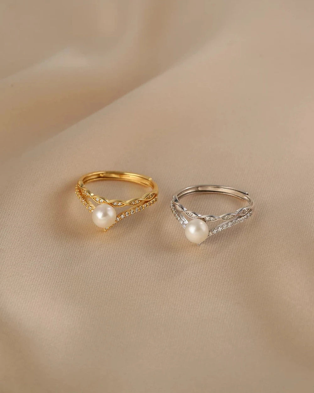 Two pearl rings, one gold and one silver, on a beige fabric background