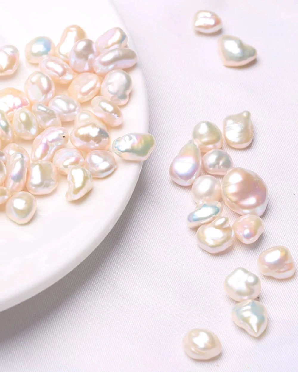 Baroque pearls on a white plate and scattered on a white surface