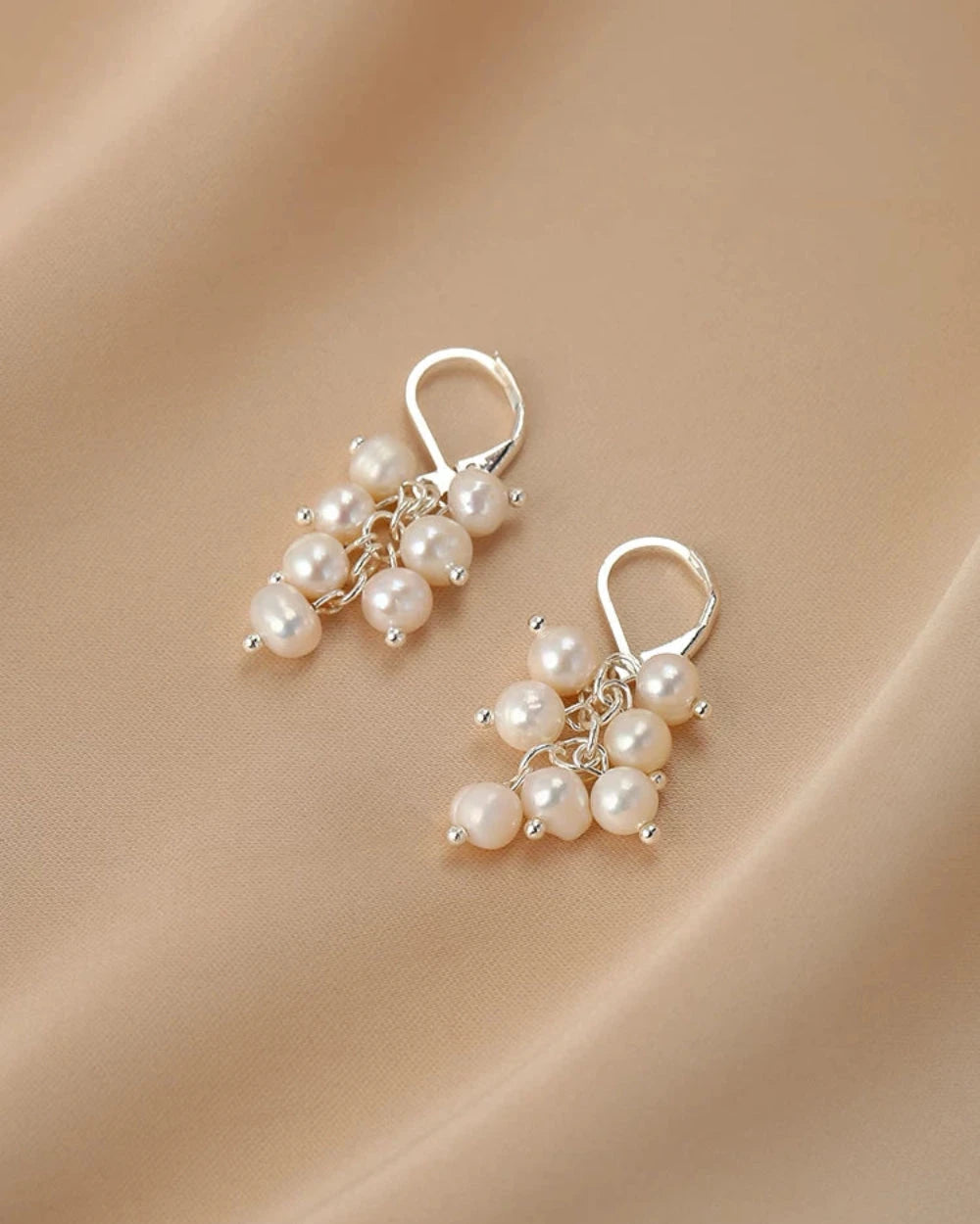 Pair of pearl earrings on a beige fabric background