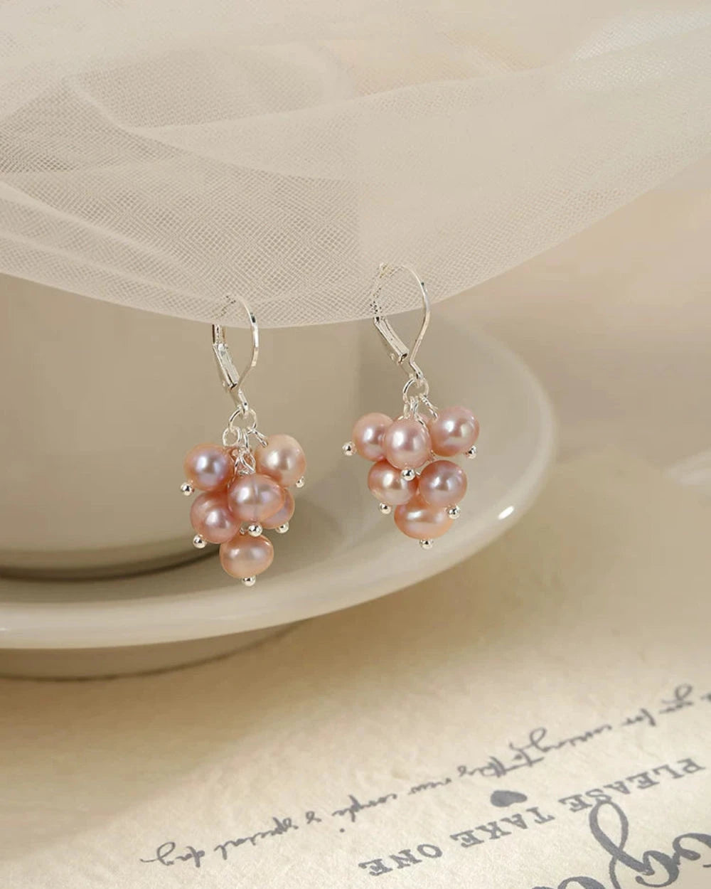 Pair of pink pearl earrings on a white dish with a soft background