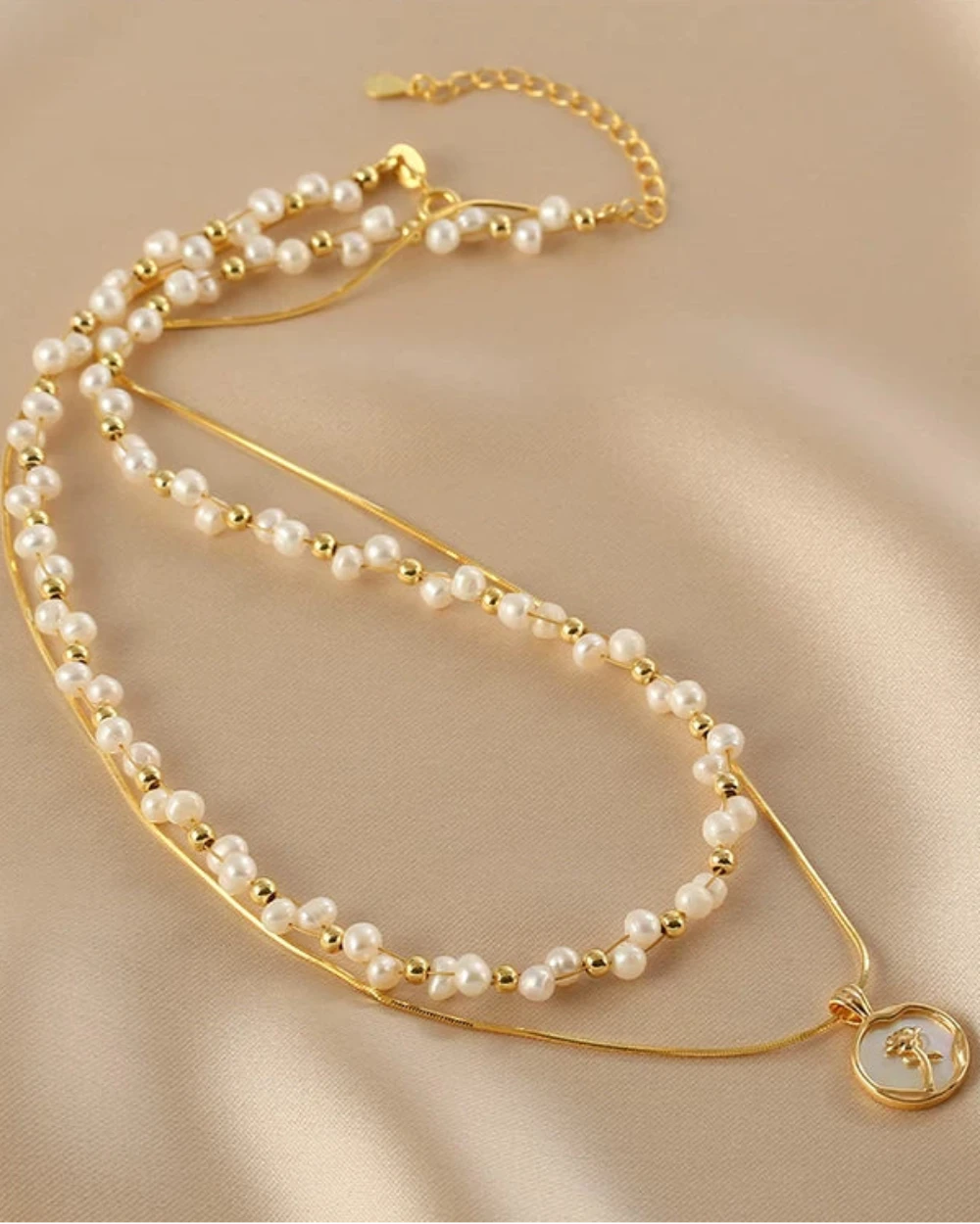 Two pearl necklaces with gold accents on a beige fabric background