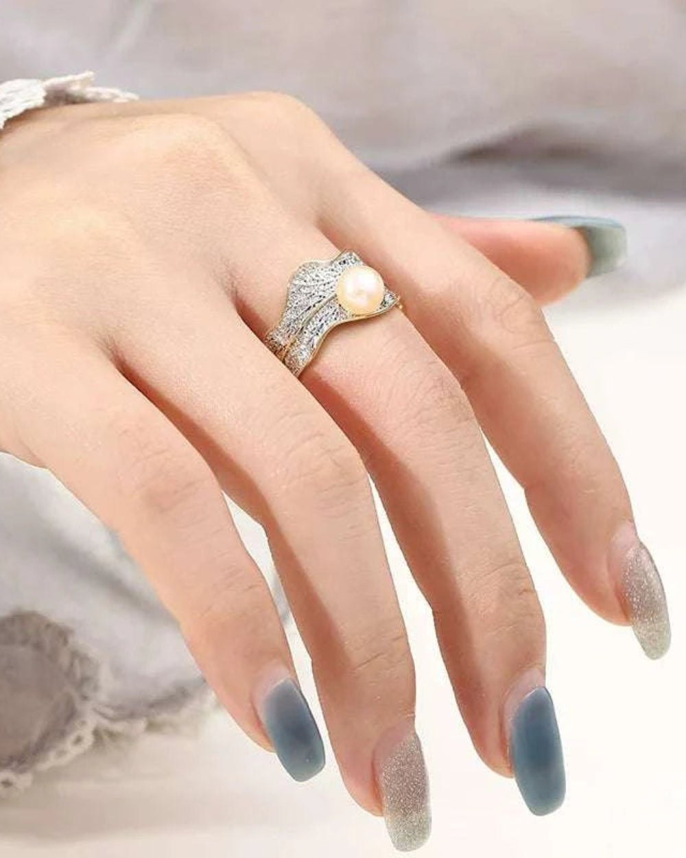 Hand wearing a silver ring with a pearl on a blurred background