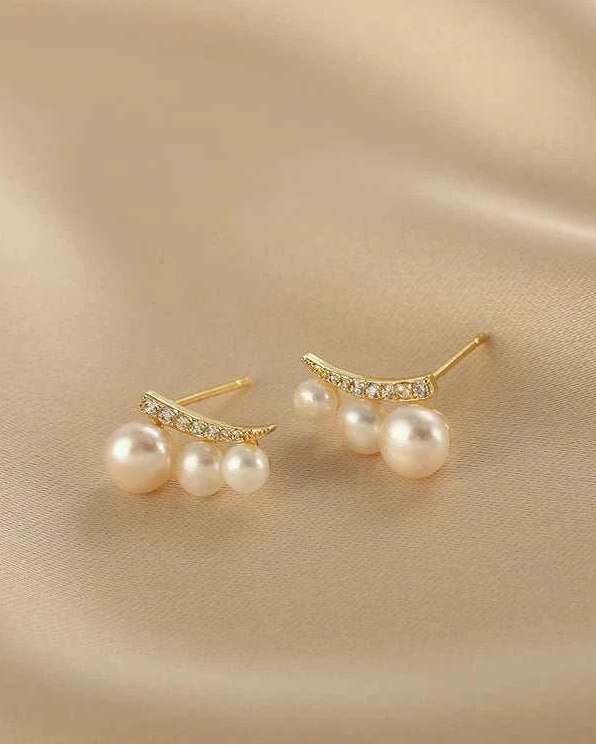 Pair of pearl earrings with gold accents on a beige fabric background