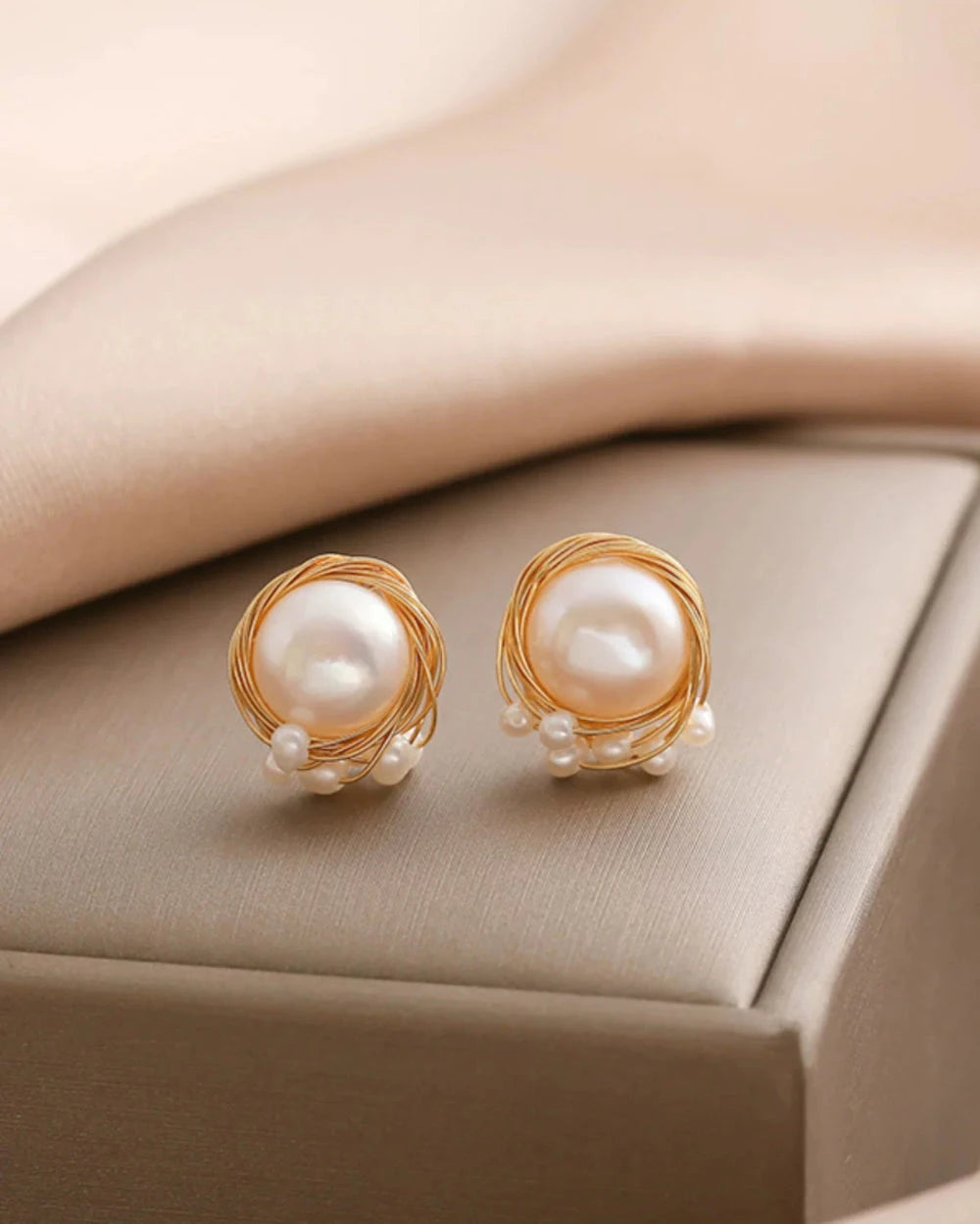 Pearl earrings with gold settings on a beige surface