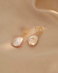 Pair of pearl earrings with gold accents on a beige fabric background