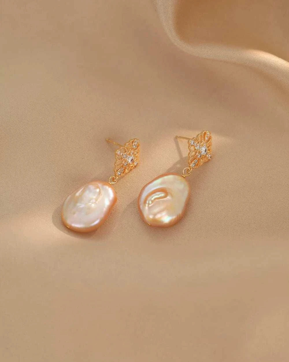 Pair of pearl earrings with gold accents on a beige fabric background