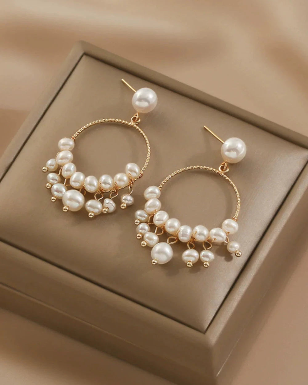 Gold hoop earrings with pearls on a beige jewelry box